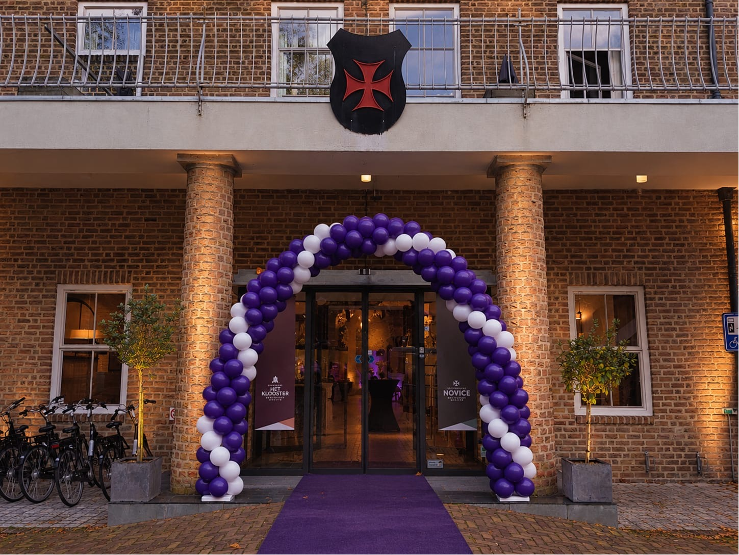 Paars-witte ballonnenboog met bijpassende loper bij een hotelingang Ballonnenservice.nl